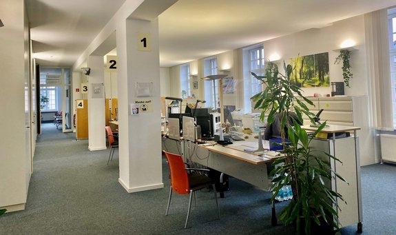 Blick in die hellen Räumlichkeiten des Bürgerbüros in Saarwellingen mit Säulen, Schreibtischen, Stühlen, Pflanzen und Bildern.