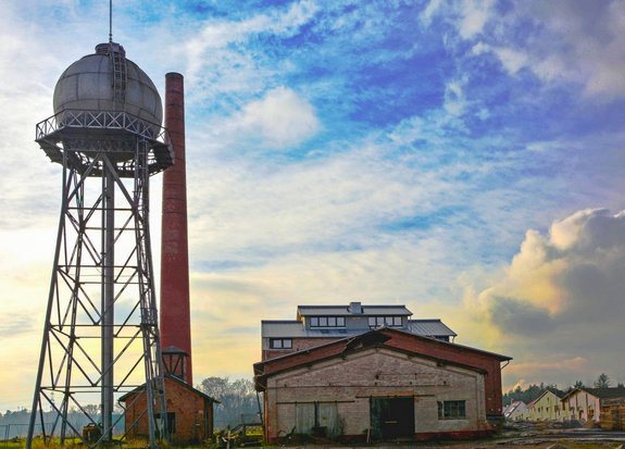 Fabrikgebäude neben einem Wasserturm. Blauer Himmel von Wolken durchzogen.