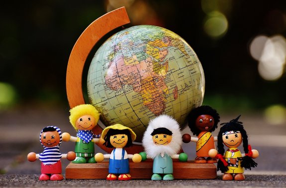 Im Hintergrund ein Globus aus Holz. Davor verschiedene Püppchen verschiedener Nationalitäten.