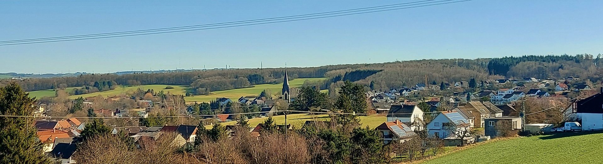 Blick über eine grüne Wiese Richtung Schwarzenholz. Ab Bildmitte sind die ersten Häuser zusehen. Schwarzenholz ist umrahmt von Natur.