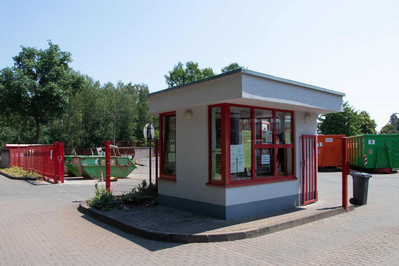 Blick auf das rot-weiße Kassenhäuschen vor dem Gelände des Wertstoffzentrums in Saarwellingen. Im Hintergrund roter Zaun und mehrere Container.