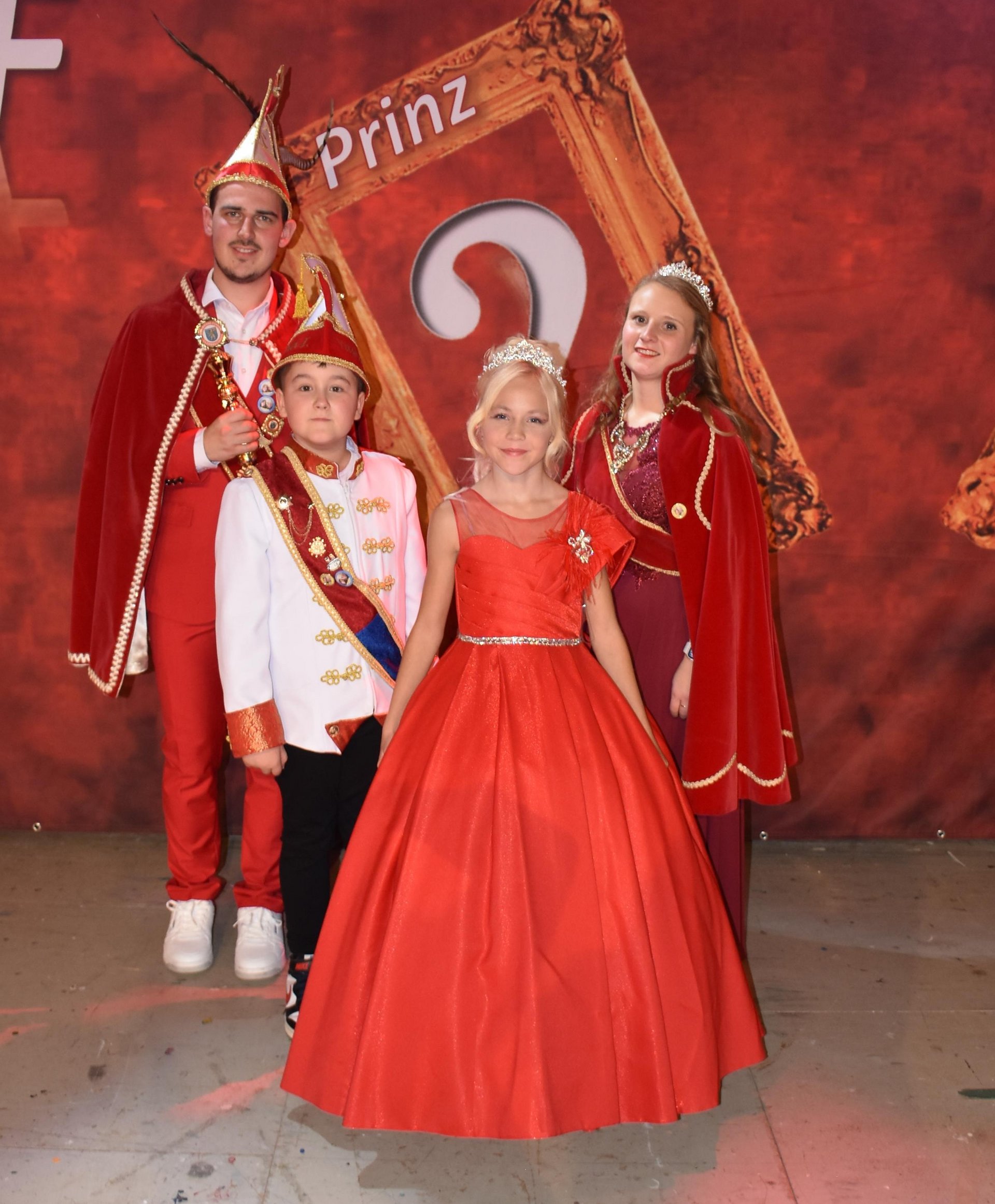 Das Bild zeigt das Fastnacht-Prinzenpaar saarwellingen der Session 2022/23. Die Prinzessin sitzt auf dem Schoß des Prinzen. Beide sind in edle, rote Gewänder gekleidet und lächeln in die Kamera.